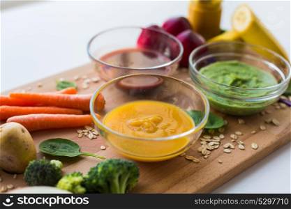 baby food, healthy eating and nutrition concept - vegetable or fruit puree in glass bowls on wooden board. vegetable puree or baby food in glass bowls