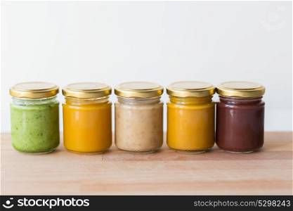 baby food, healthy eating and nutrition concept - vegetable or fruit puree or baby food in glass jars on wooden board. vegetable or fruit puree or baby food in jars