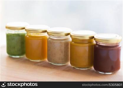 baby food, healthy eating and nutrition concept - vegetable or fruit puree or baby food in glass jars on wooden board. vegetable or fruit puree or baby food in jars