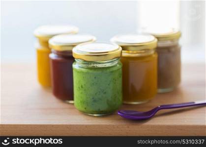 baby food, healthy eating and nutrition concept - vegetable or fruit puree in glass jars and feeding spoon on wooden board. vegetable or fruit puree or baby food in jars