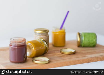 baby food, healthy eating and nutrition concept - vegetable or fruit puree in glass jars and feeding spoon on wooden board. vegetable or fruit puree or baby food in jars