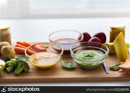 baby food, healthy eating and nutrition concept - vegetable or fruit puree in glass bowls on wooden board. vegetable puree or baby food in glass bowls