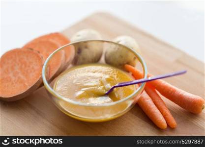 baby food, healthy eating and nutrition concept - vegetable puree in bowl with feeding spoon on wooden board. vegetable puree or baby food in bowl with spoon