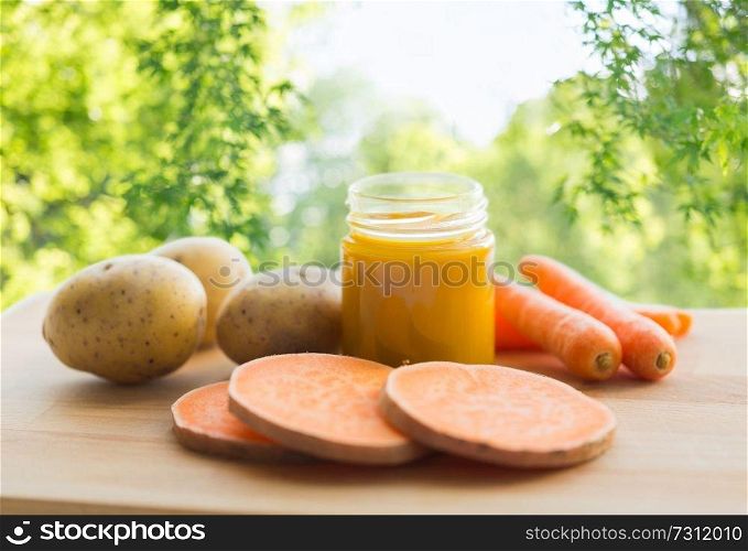 baby food, healthy eating and nutrition concept - vegetable puree in glass jar on wooden board over green natural background. vegetable puree or baby food in glass jar