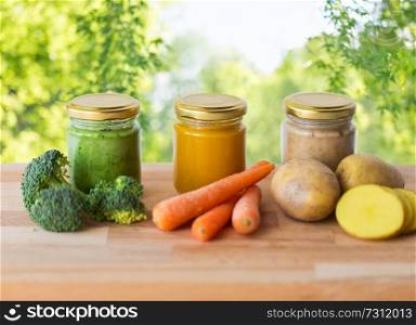 baby food, healthy eating and nutrition concept - vegetable puree in glass jars on wooden table over green natural background. vegetable puree or baby food in glass jars