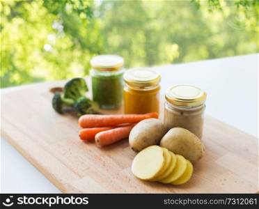 baby food, healthy eating and nutrition concept - vegetable puree in glass jars on wooden board over green natural background. vegetable puree or baby food in glass jars
