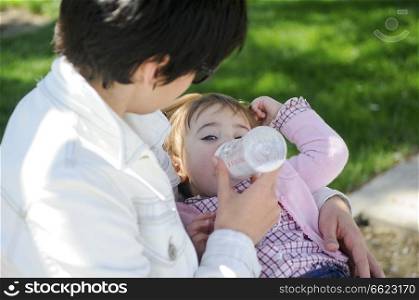 Baby girl drinking milk from baby bottle. Mother feeding daughter from bottle.