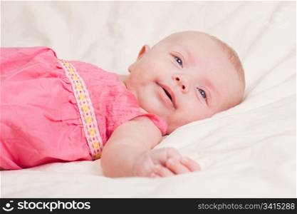 Baby girl in pink dress lying on bed