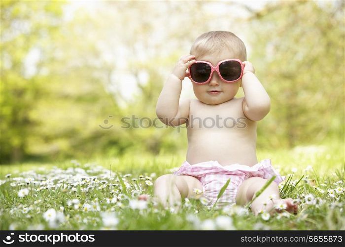 Baby Girl In Summer Dress Sitting In Field Wearing Sunglasses