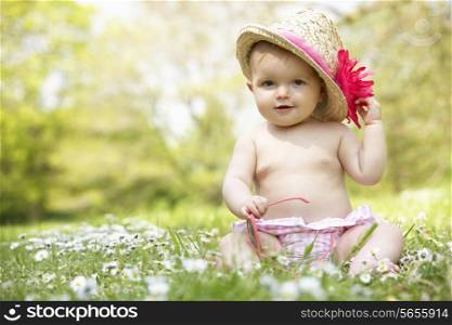 Baby Girl In Summer Dress Sitting In Field Wearing Sunglasses And Straw Hat