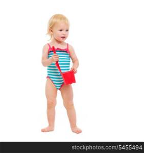 Baby girl in swimsuit holding bucket and shovel looking in corner