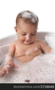 Baby girl is looking at bubbles in bathtub with foam on her head