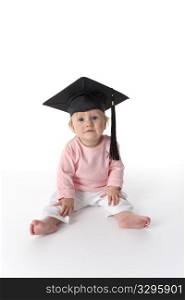Baby girl is sitting on the floor with a graduation cap on white background