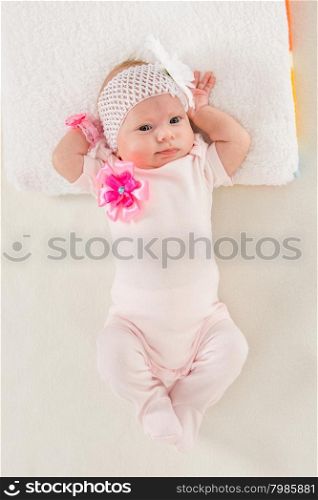Baby girl lying in bed stretching. a two-month baby girl Europeans on the back with a bandage on his head with a flower lying on a soft bed