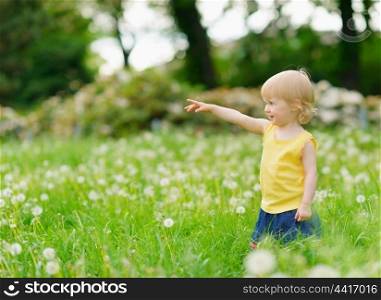 Baby girl on dandelions field pointing on copy space