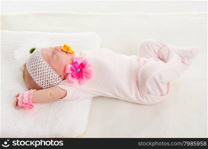 Baby girl stretches in his sleep lying in bed. a two-month baby girl Europeans on the back with a bandage on his head with a flower lying on a soft bed