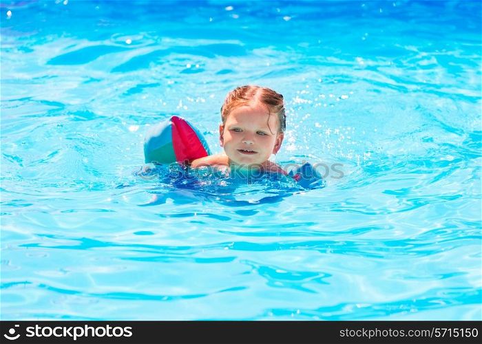 Baby girl swimming in blue pool with floats sleeves at summer vacation