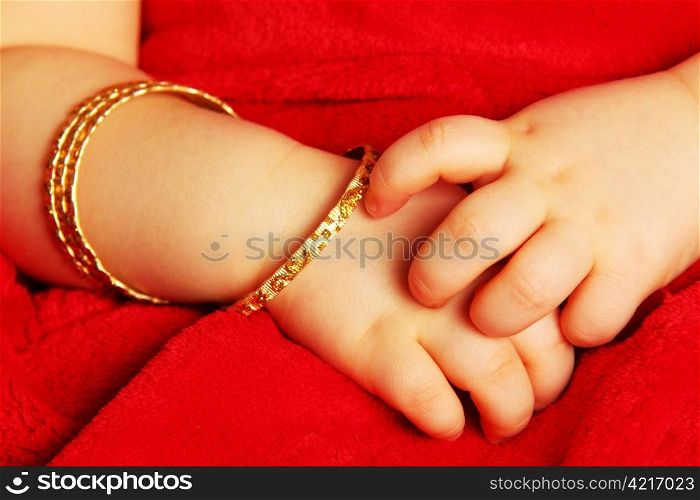 Baby hands. Baby hands with bracelets of yellow gold, isolated towards dark red
