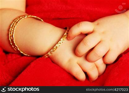 Baby hands. Baby hands with bracelets of yellow gold, isolated towards dark red
