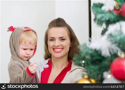 Baby helping mother decorate Christmas tree