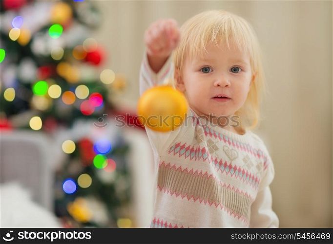 Baby holding Christmas ball near Christmas tree