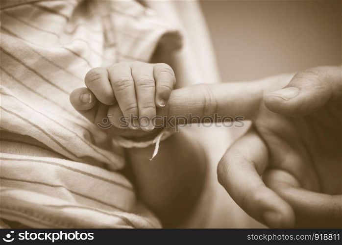 Baby holding mother fingers in concept of love and family. Closeup baby and mom palm hands. Newborn and infant tenderness. Health and trust of relationship people. Vintage tone film