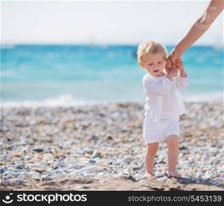 Baby holding mothers hand and walking on beach