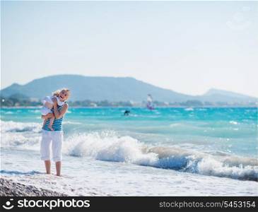 Baby hugging mother standing at sea shore