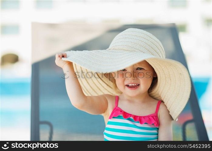 Baby in beach hat sitting on sun bed
