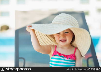 Baby in beach hat sitting on sun bed