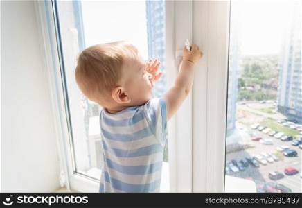 Baby in danger. Baby boy pulling handle of window