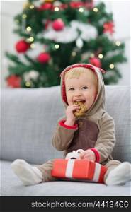 Baby in deer suit with Christmas present box eating cookie