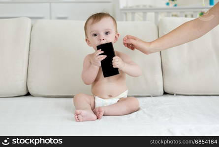 Baby in diapers sitting on bed and holding smartphone