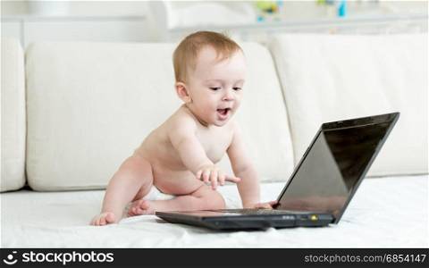 Baby in diapers sitting on bed and using laptop