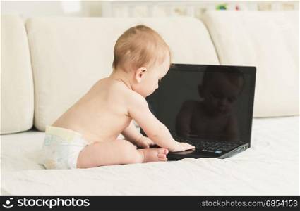Baby in diapers sitting on bed and using laptop