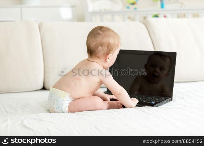 Baby in diapers sitting on bed with laptop