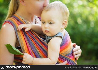 Baby in sling outdoor. Mother is carrying her child and showing nature details. Baby in sling