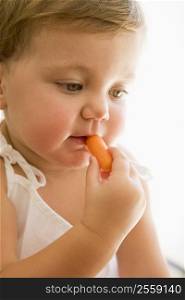 Baby indoors eating carrot.