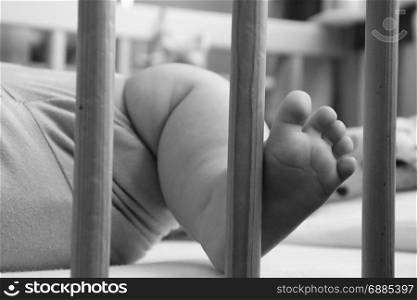 Baby, infant feet sticking out through the rails of a crib, cot, black and white photo, beautiful background for card, banner, wallpaper design