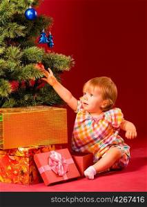 baby is reaching for christmas toy near tree