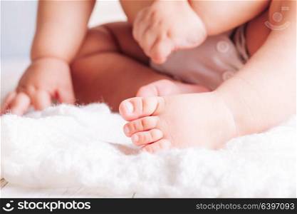 Baby is sitting on the textile. Hands and feet close up. Baby hands and foot