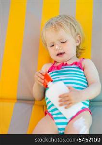 Baby laying on sun bed with sun block bottle