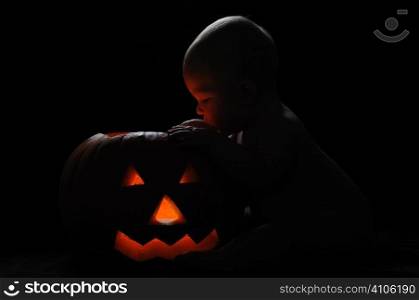 Baby looking into a lit up pumpkin at halloween