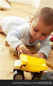 Baby lying on front playing with blocks and truck