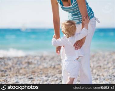 Baby on beach climbing mothers hands