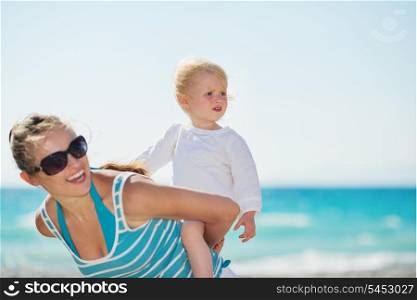 Baby on beach piggybacking mother and looking on copy space