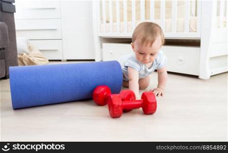 Baby playing on floor with fitness mat and dumbbells. Concept of child sports
