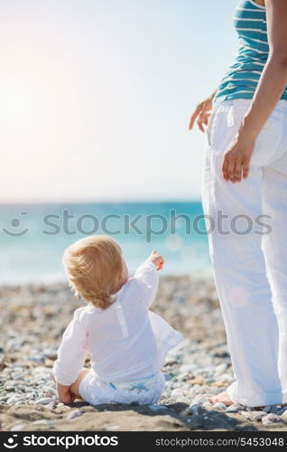 Baby showing mother something on beach. Rear view