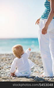 Baby showing mother something on beach. Rear view