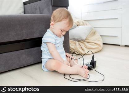 Baby sitting alone in living room and playing with electrical cables